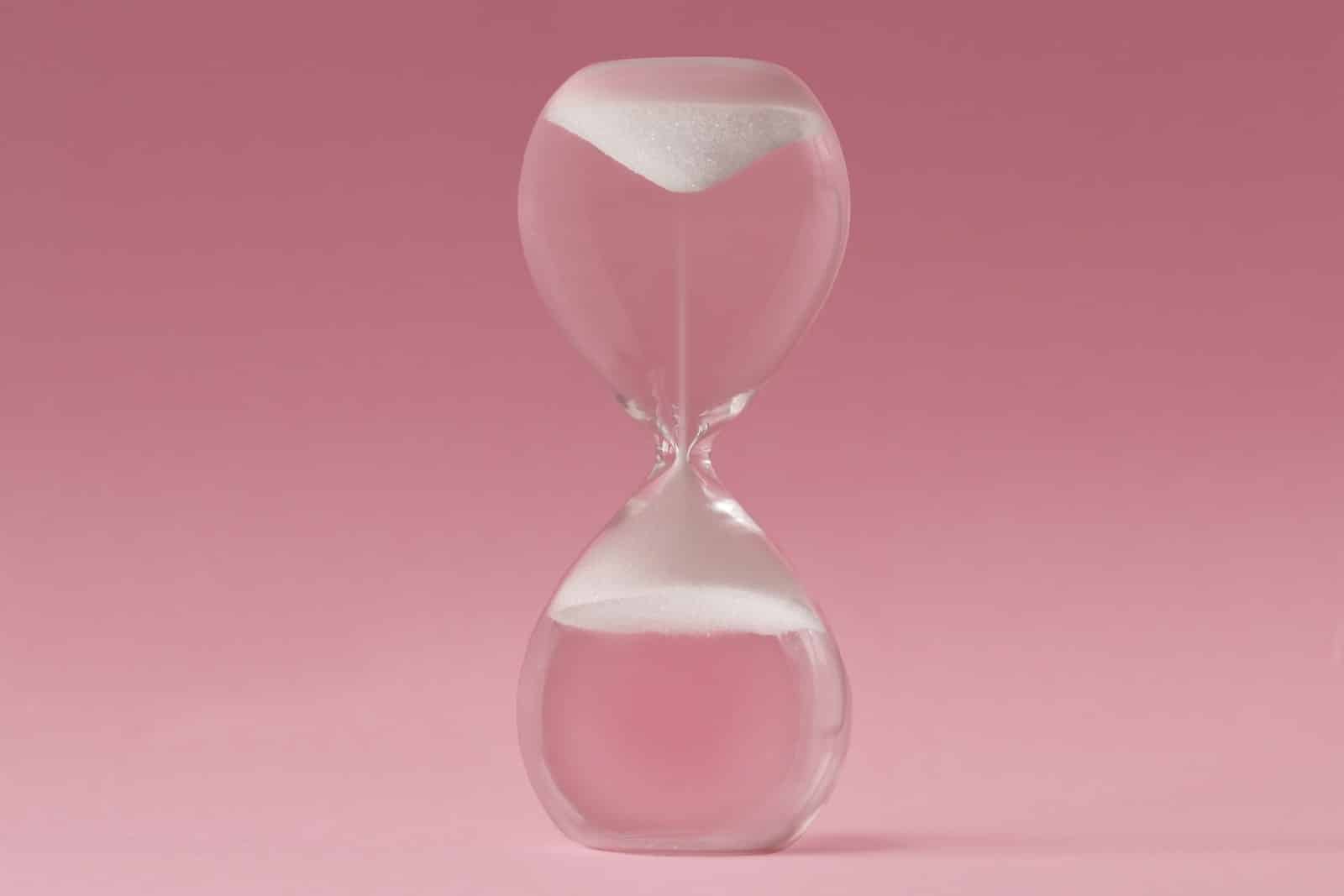 reverse aging upside down hourglass turning back time pink background