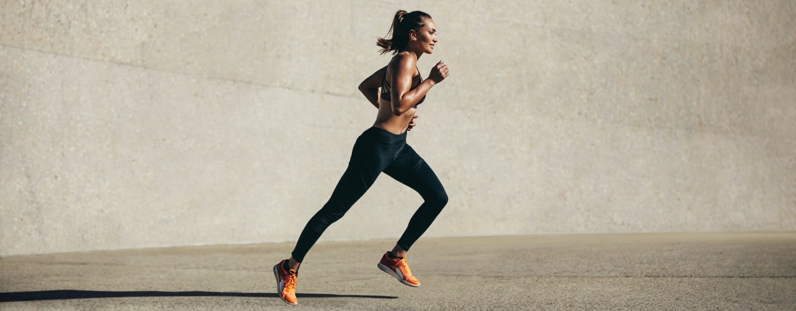 healthy young woman exercising in front of concrete wall wearing black trousers