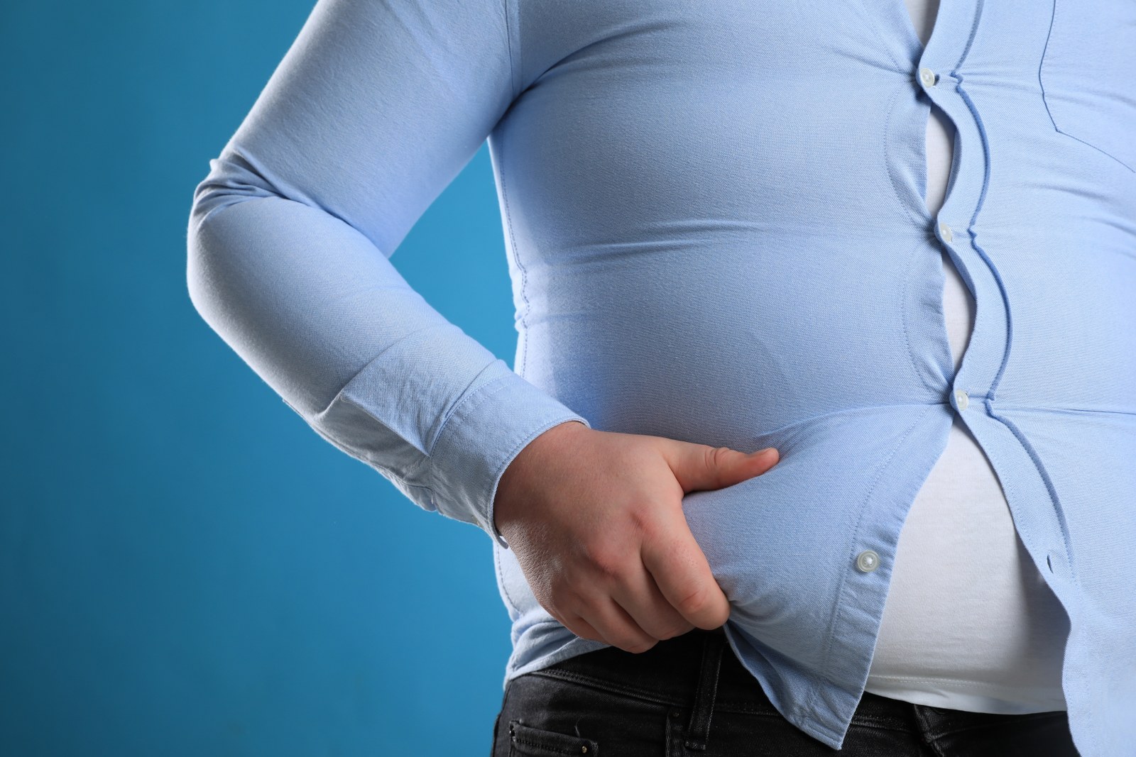 overweight obesity diabetes beer belly love handles hand grabbing blue shirt and belly